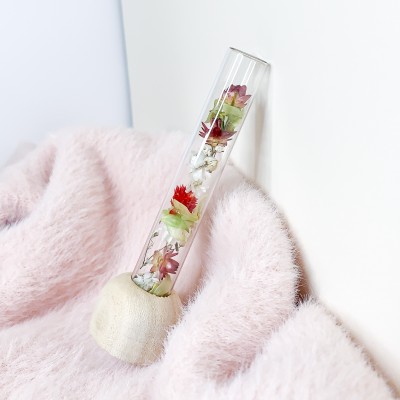 Tube en verre contenant un mélange de fleurs séchées. Format moyen.