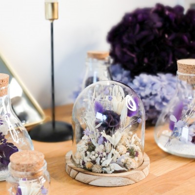 Cloche en verre et base en bois contenant des fleurs séchées crème, parme et violet. Petit format. Collection Milka