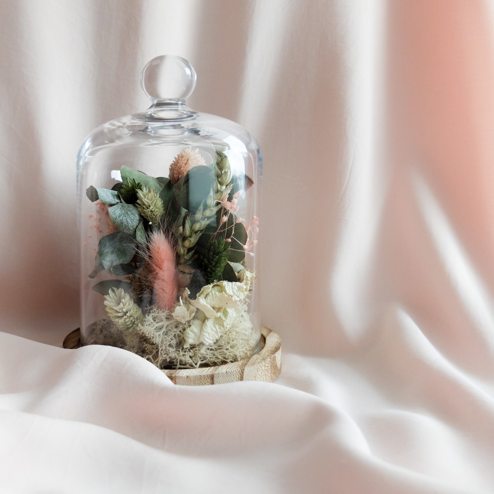Cloche en verre et base en bois contenant des fleurs séchées crème, rose et vert. Petit format.