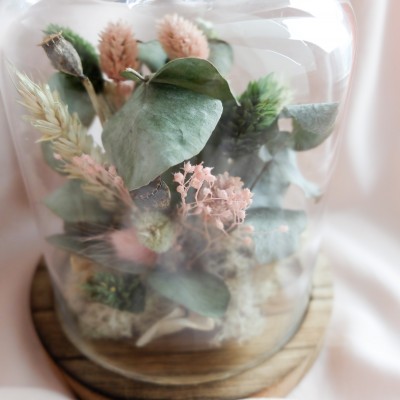 Cloche en verre et base en bois contenant des fleurs séchées crème, rose et vert. Petit format.