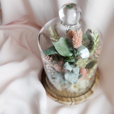 Cloche en verre et base en bois contenant des fleurs séchées crème, rose et vert. Petit format.