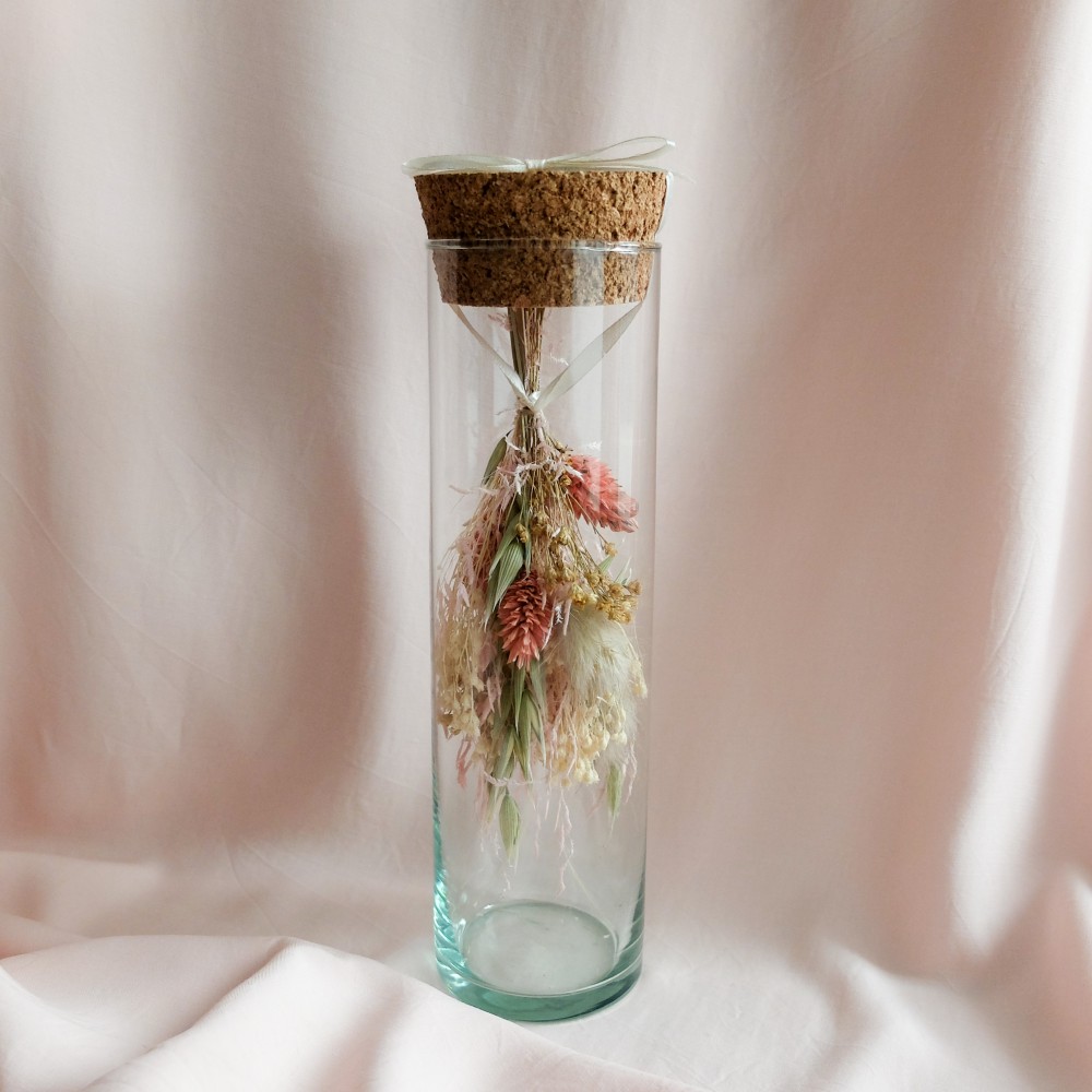 Fiole en verre contenant un bouquet suspendu crème, rose et vert.
