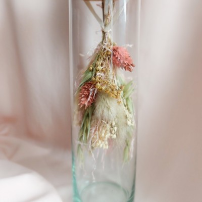 Fiole en verre contenant un bouquet suspendu crème, rose et vert.