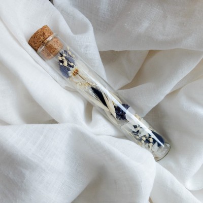 Tube en verre contenant des fleurs séchées blanc et bleu. Petit format.