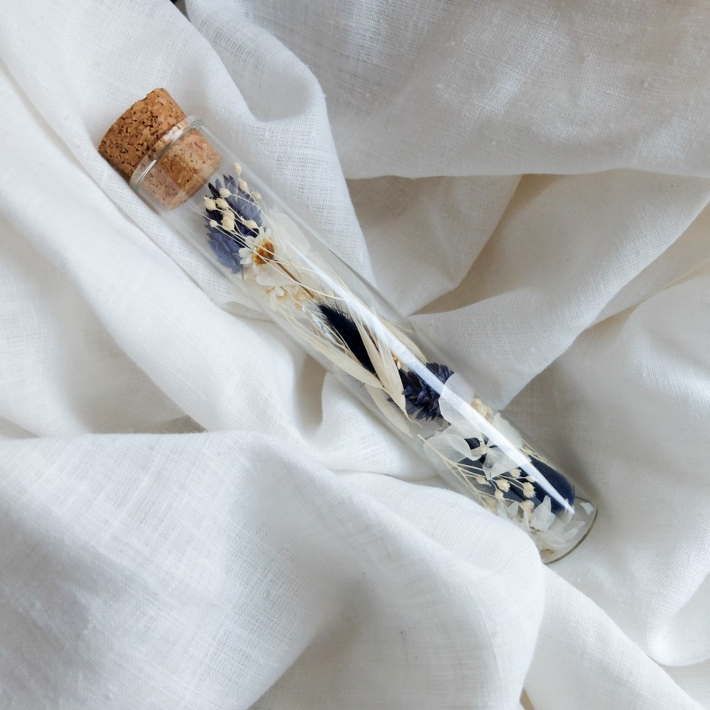 Tube en verre contenant des fleurs séchées blanc et bleu. Petit format.