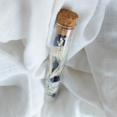 Tube en verre contenant des fleurs séchées blanc et bleu. Petit format.