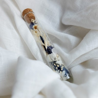Tube en verre contenant des fleurs séchées blanc et bleu. Petit format.