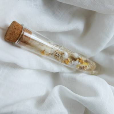 Tube en verre contenant des fleurs séchées blanc et jaune. Petit format.