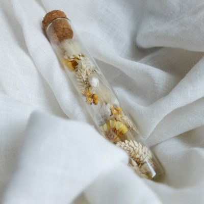 Tube en verre contenant des fleurs séchées blanc et jaune. Petit format.