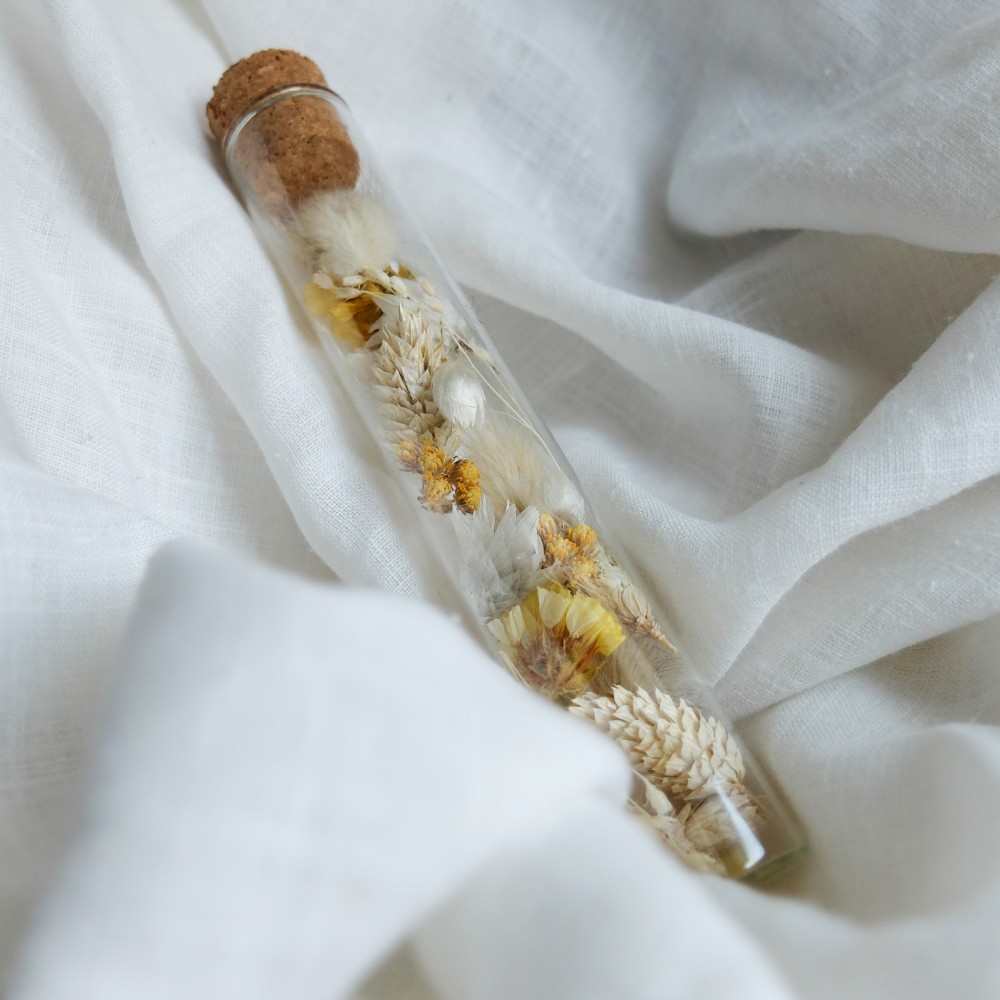 Tube en verre contenant des fleurs séchées blanc et jaune. Petit format.