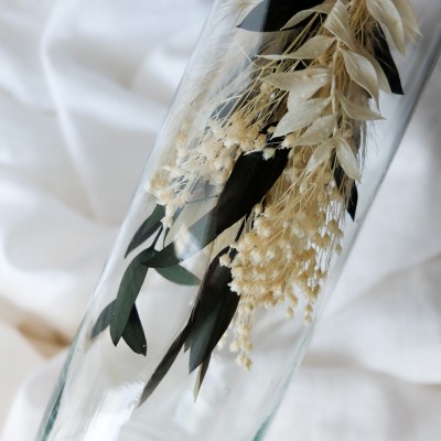 Fiole en verre contenant un bouquet suspendu crème et vert.