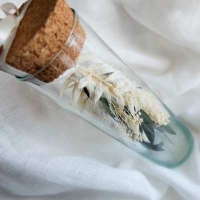 Fiole en verre contenant un bouquet suspendu crème et vert.