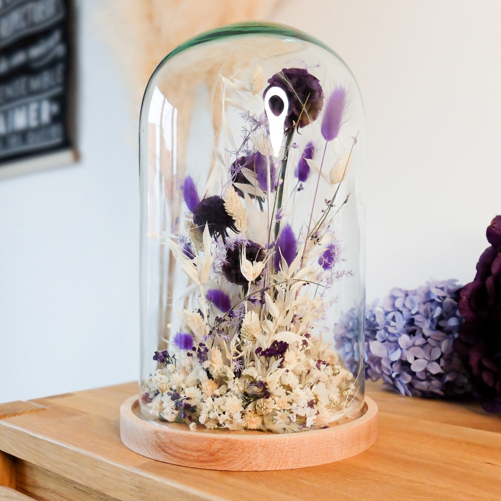 Cloche en verre et base en bois contenant des fleurs séchées blanches et violettes