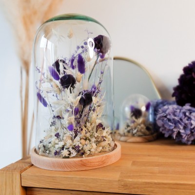 Cloche en verre et base en bois contenant des fleurs séchées blanches et violettes