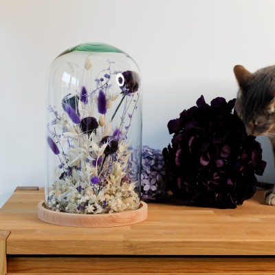 Cloche en verre et base en bois contenant des fleurs séchées blanches et violettes
