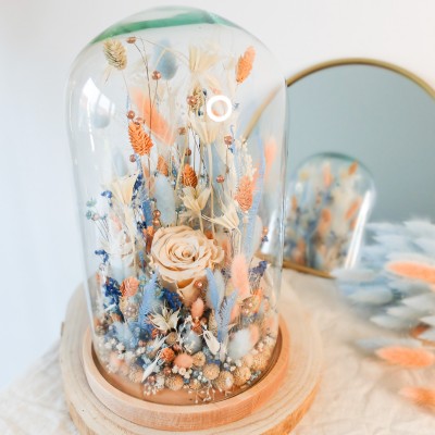 Cloche en verre et base en bois contenant des fleurs séchées blanches, pêche et bleu ciel. Grand format. Collection Pêche Bleue