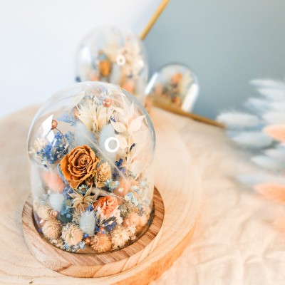 Cloche en verre et base en bois contenant des fleurs séchées blanches, pêche et bleu ciel. Petit format. Collection Pêche Bleue