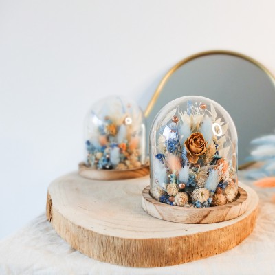 Cloche en verre et base en bois contenant des fleurs séchées blanches, pêche et bleu ciel. Petit format. Collection Pêche Bleue