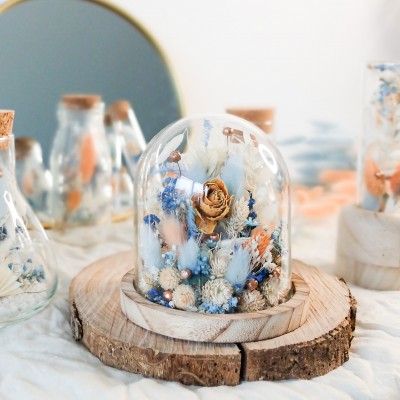 Cloche en verre et base en bois contenant des fleurs séchées blanches, pêche et bleu ciel. Petit format. Collection Pêche Bleue