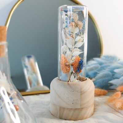 Tube en verre contenant des fleurs séchées blanches, pêche et bleu ciel. Format moyen.