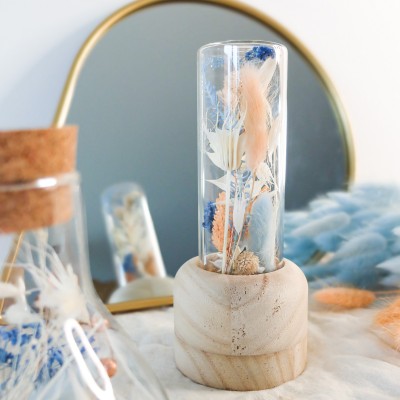 Tube en verre contenant des fleurs séchées blanches, pêche et bleu ciel. Format moyen.