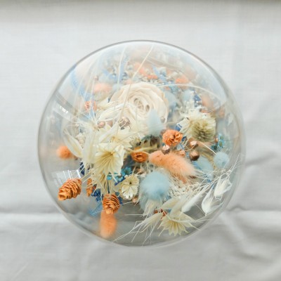 Cloche en verre et base en bois contenant des fleurs séchées blanches, pêche et bleu ciel. Grand format. Collection Pêche Bleue